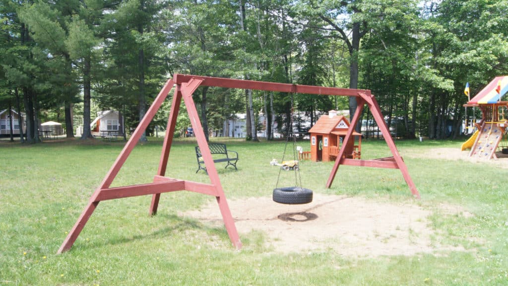 Chain O' Lakes Campground -- the playground against a backdrop of trees and a lake.